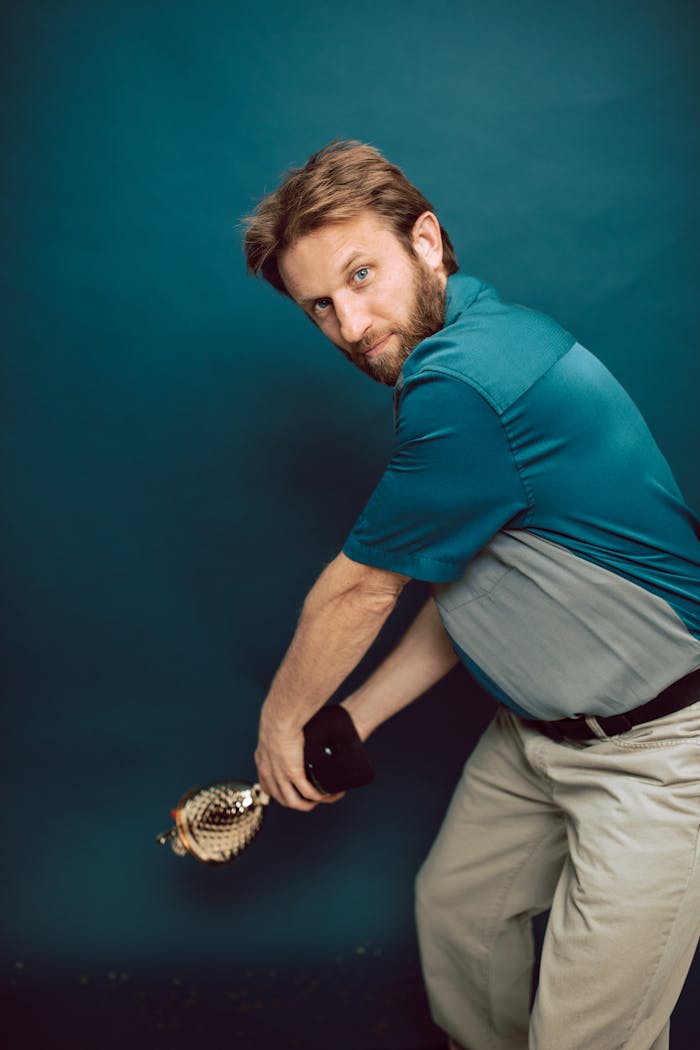 A man striking a dynamic pose while holding a trophy against a blue background.