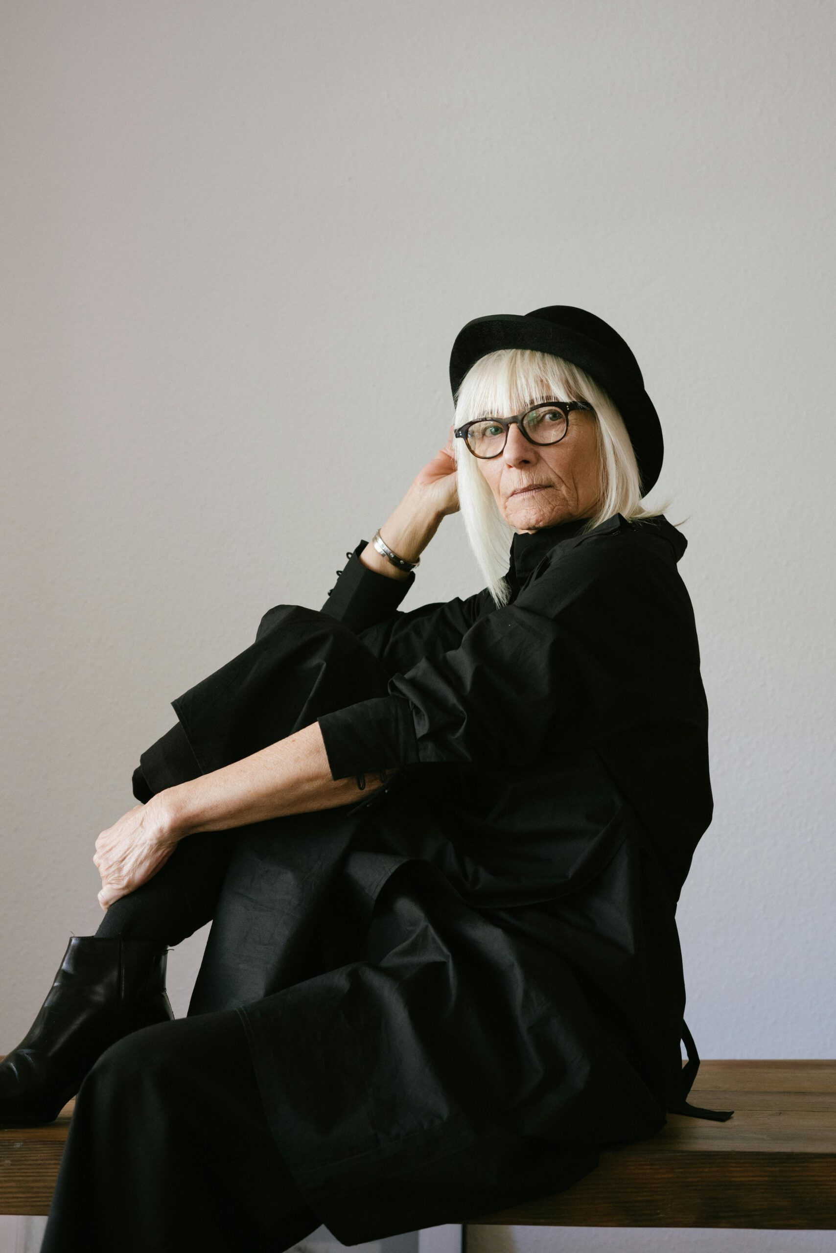 Elegant senior woman wearing eyeglasses and a black outfit posing indoors, showcasing timeless fashion.