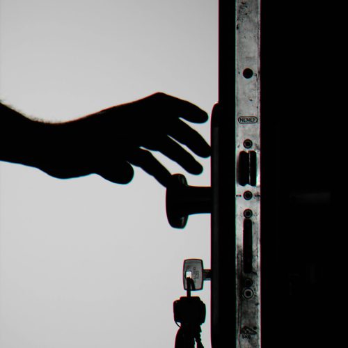 Silhouette of a hand about to open a door with keys in lock, symbolizing security.